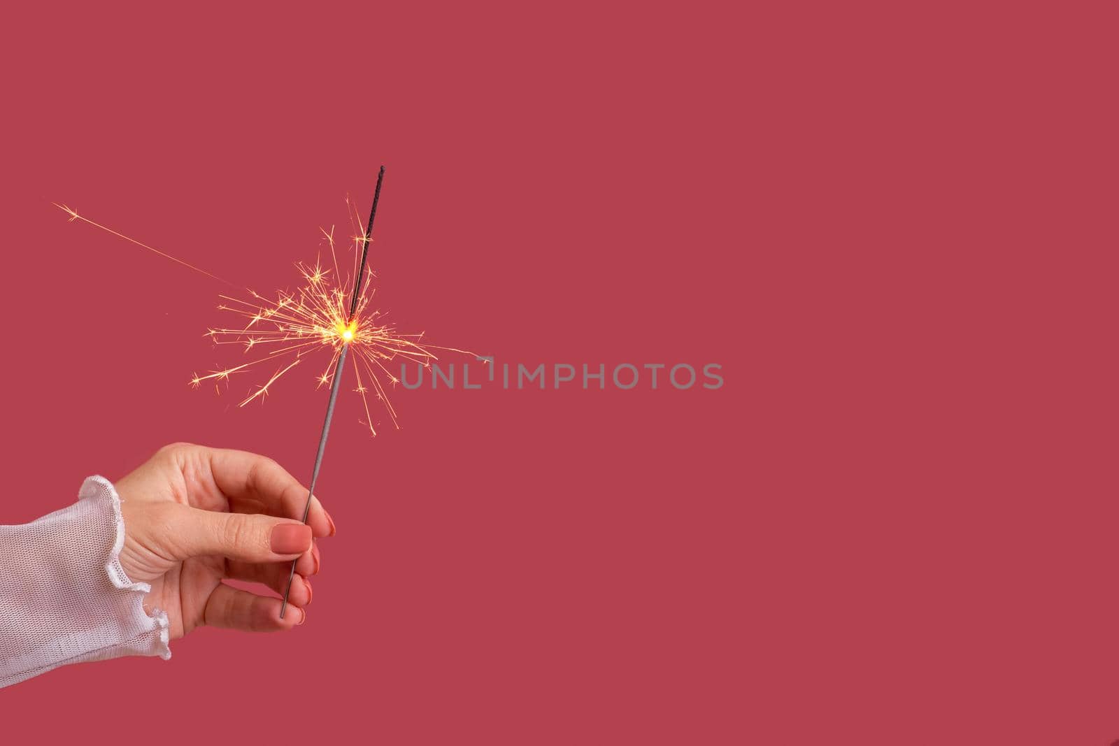 Bengal fire in female hand on a colored background. Minimalistic christmas festive concept with copy space.