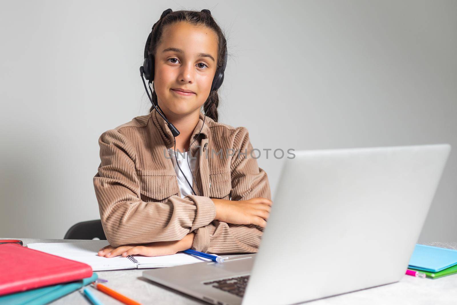 Smiling little Caucasian girl in headphones handwrite study online using laptop at home, cute happy small child in earphones take Internet web lesson or class on computer, homeschooling concept.