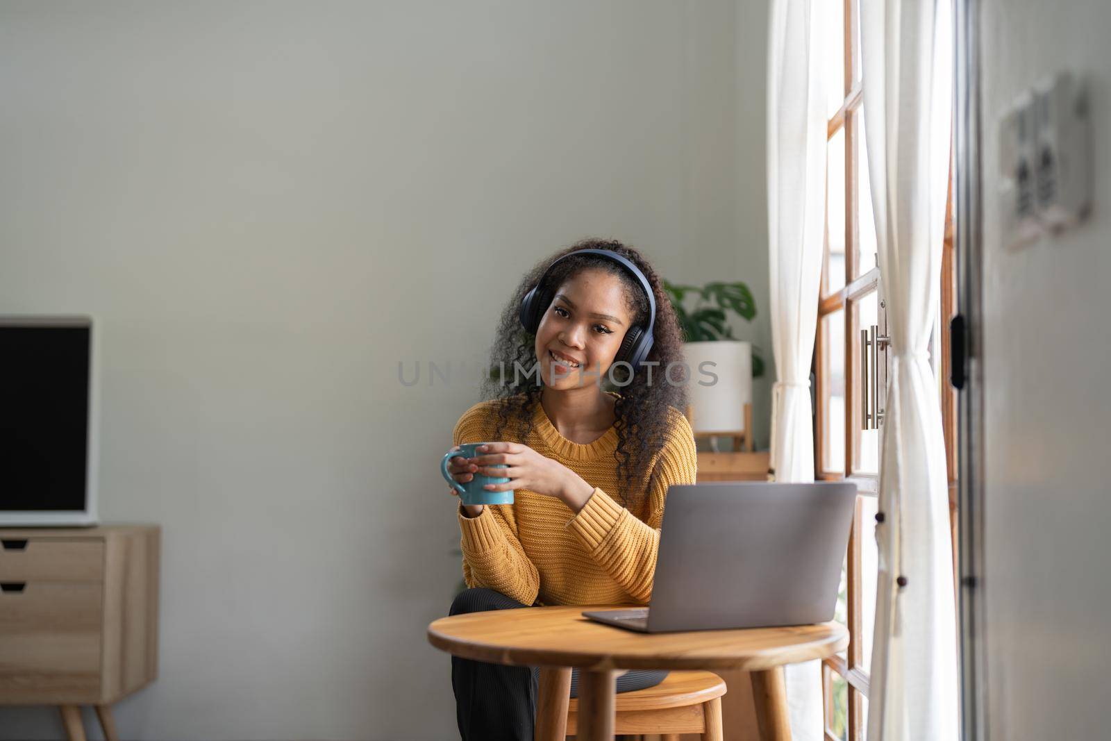 Portrait of African American woman talking on video conference call using laptop and headphones taking notes on notepad. Brunette sits at table in home office