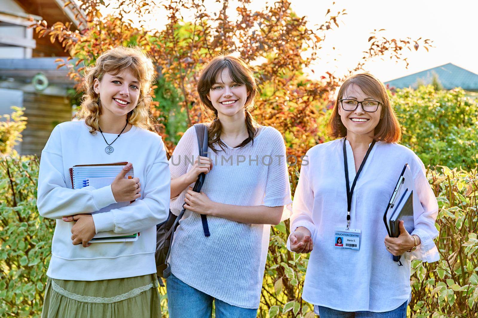 Outdoor portrait of a female educator and two teenage female students, smiling, looking at the camera. Teaching, education, youth, high school, college, university concept