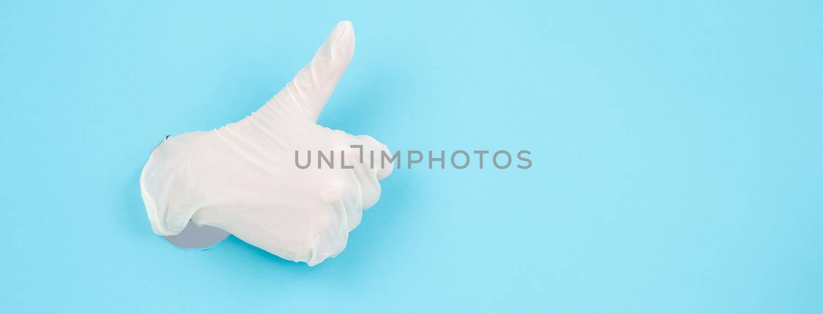 A female gloved hand sticks out through a blue paper background and shows a thumbs up. Widescreen