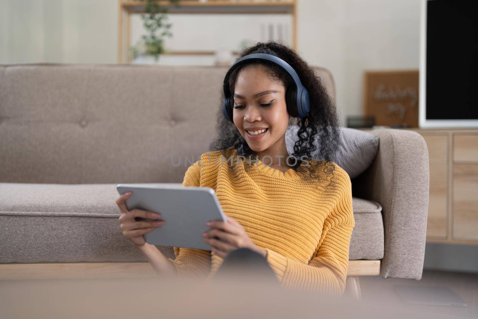 Portrait of young smiling black woman in wireless headset holding using digital tablet sitting in living room. by nateemee