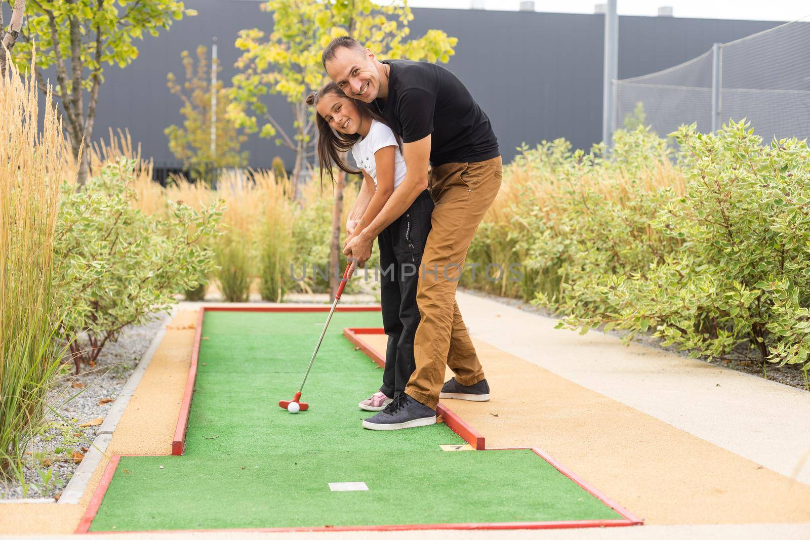 father and daughter playing mini golf together in the park.