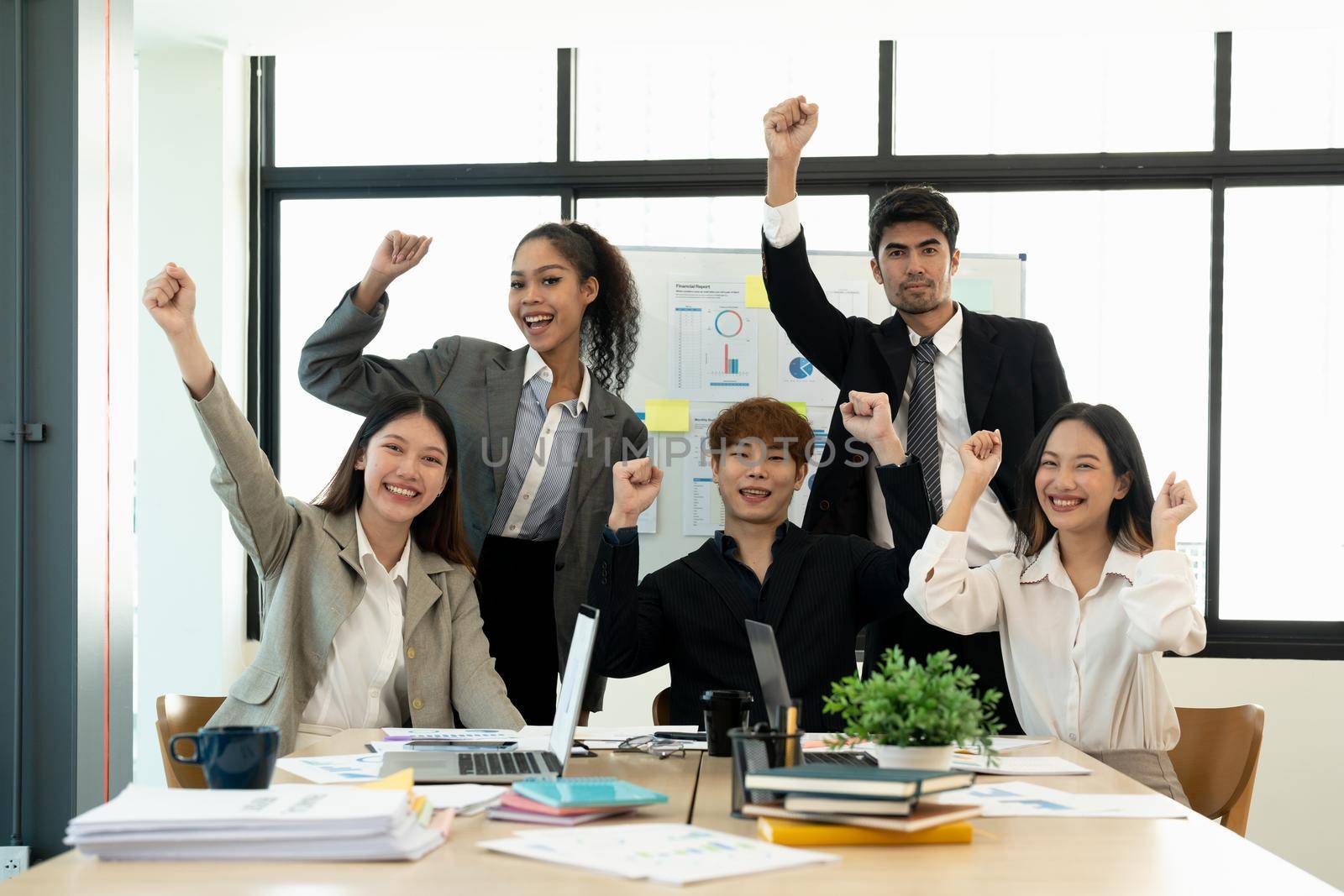 Portrait success and team work concept. Group of business partners with raised up hands in light modern workstation, celebrating the breakthrough in their company.