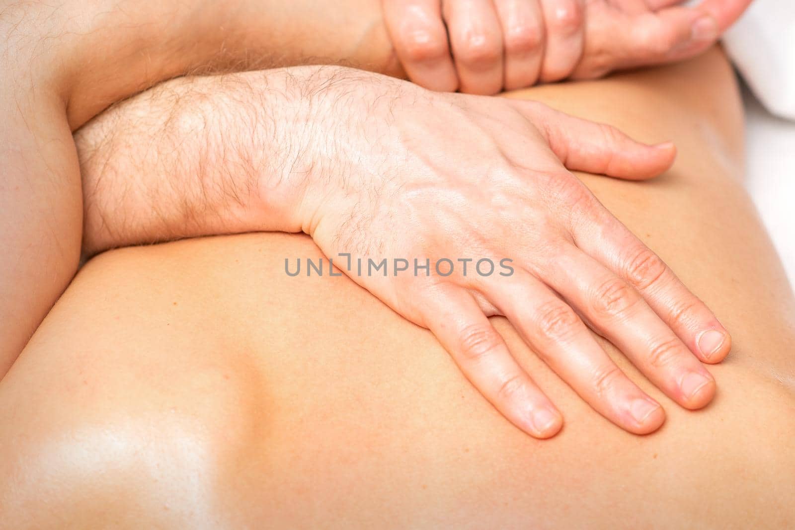A male physiotherapist stretches the arms on the back of a man lying down, close up