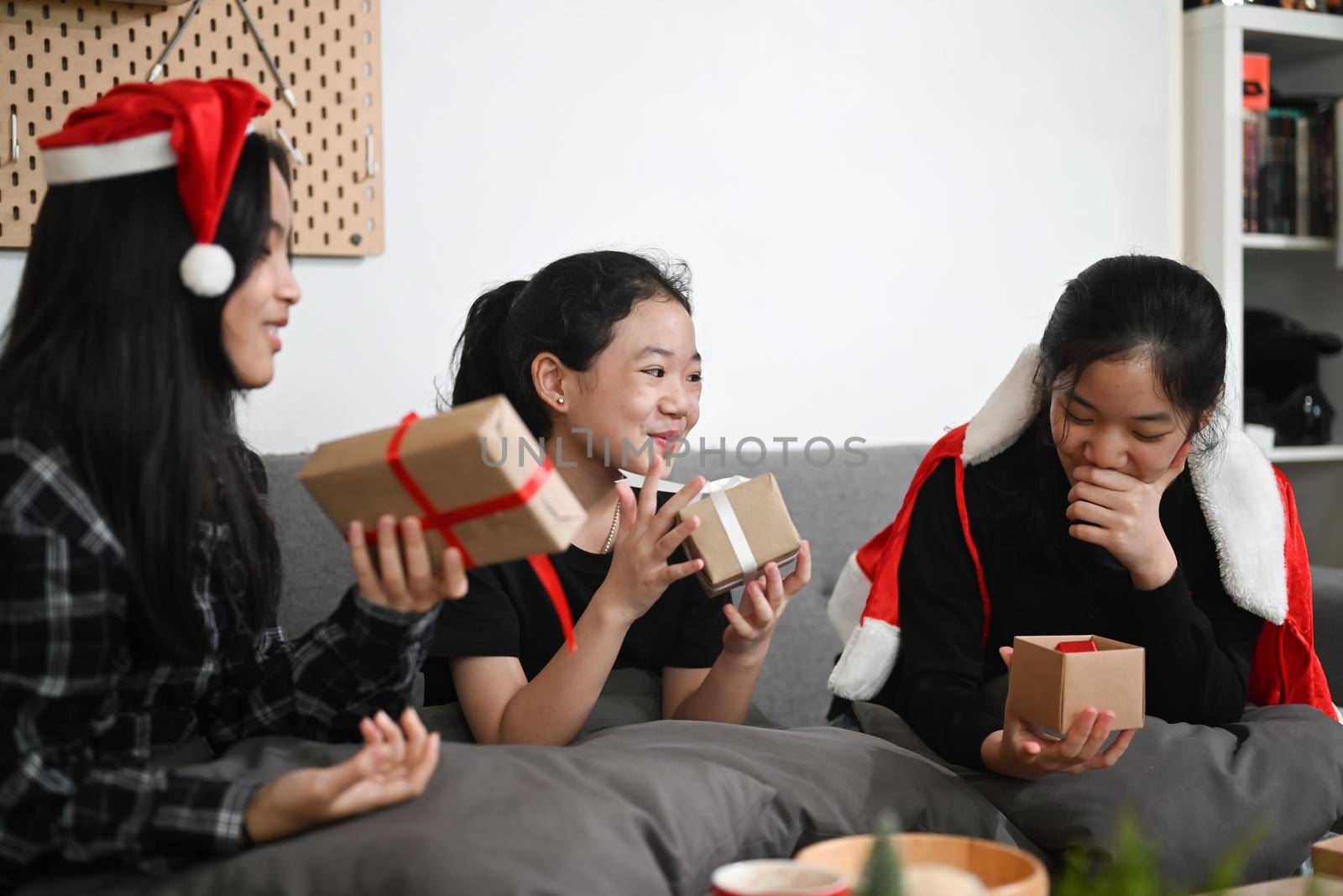 Cheerful cute children girls having fun opening gifts near Christmas tree in living room.