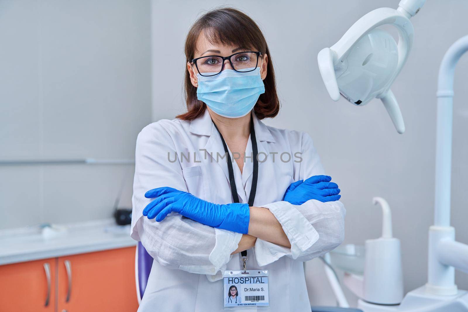 Portrait of serious female doctor dentist in face mask in office. Confident middle aged woman looking at camera with crossed arms near dental chair. Dentistry medicine, specialist, career, health care