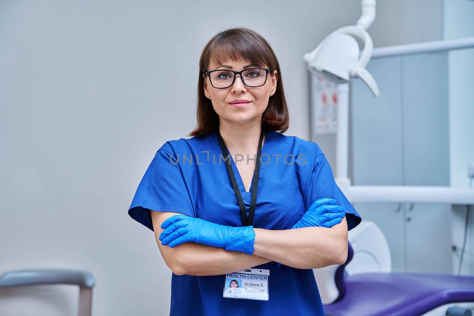 Portrait of female doctor dentist in office. Confident middle aged woman looking at camera with crossed arms near dental chair. Dentistry, medicine, specialist, career, dental health care concept