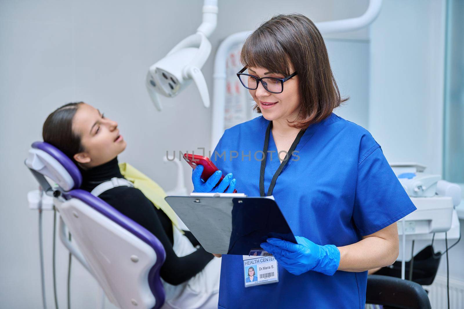 Female dentist, nurse doctor with clipboard phone in dental office by VH-studio