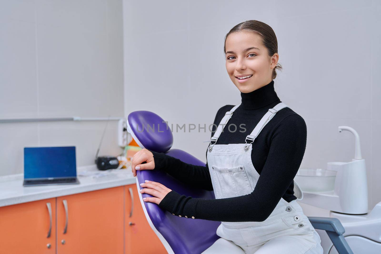 Portrait of young smiling teenage girl in dental chair looking at camera by VH-studio