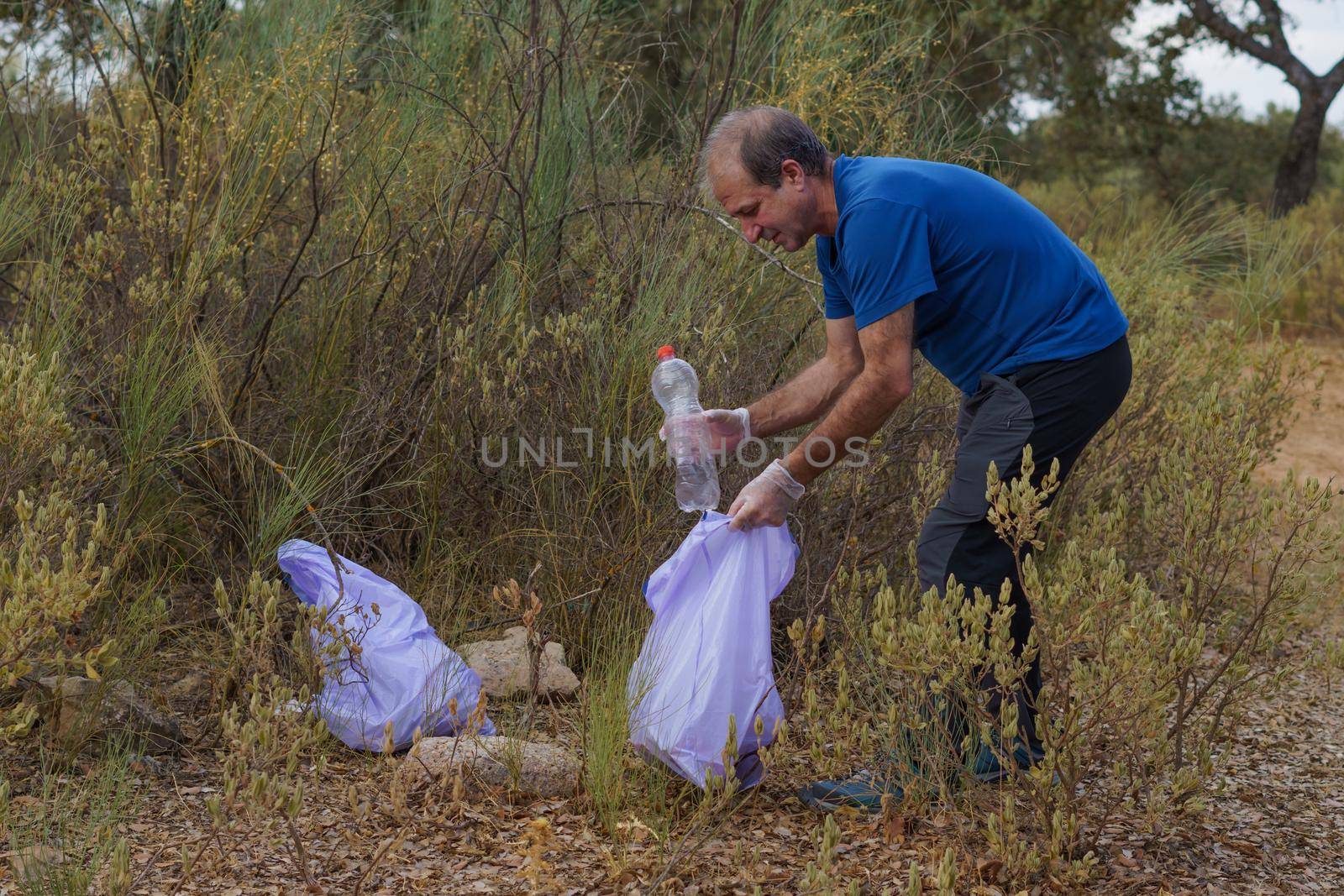man with garbage bags and gloves cleaning the bush from polluting debris