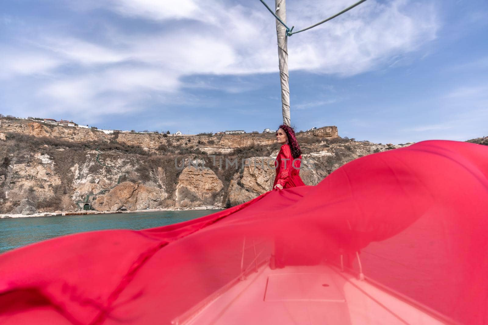 Attractive middle-aged woman in a red dress on a yacht on a summer day. Luxury summer adventure, outdoor activities