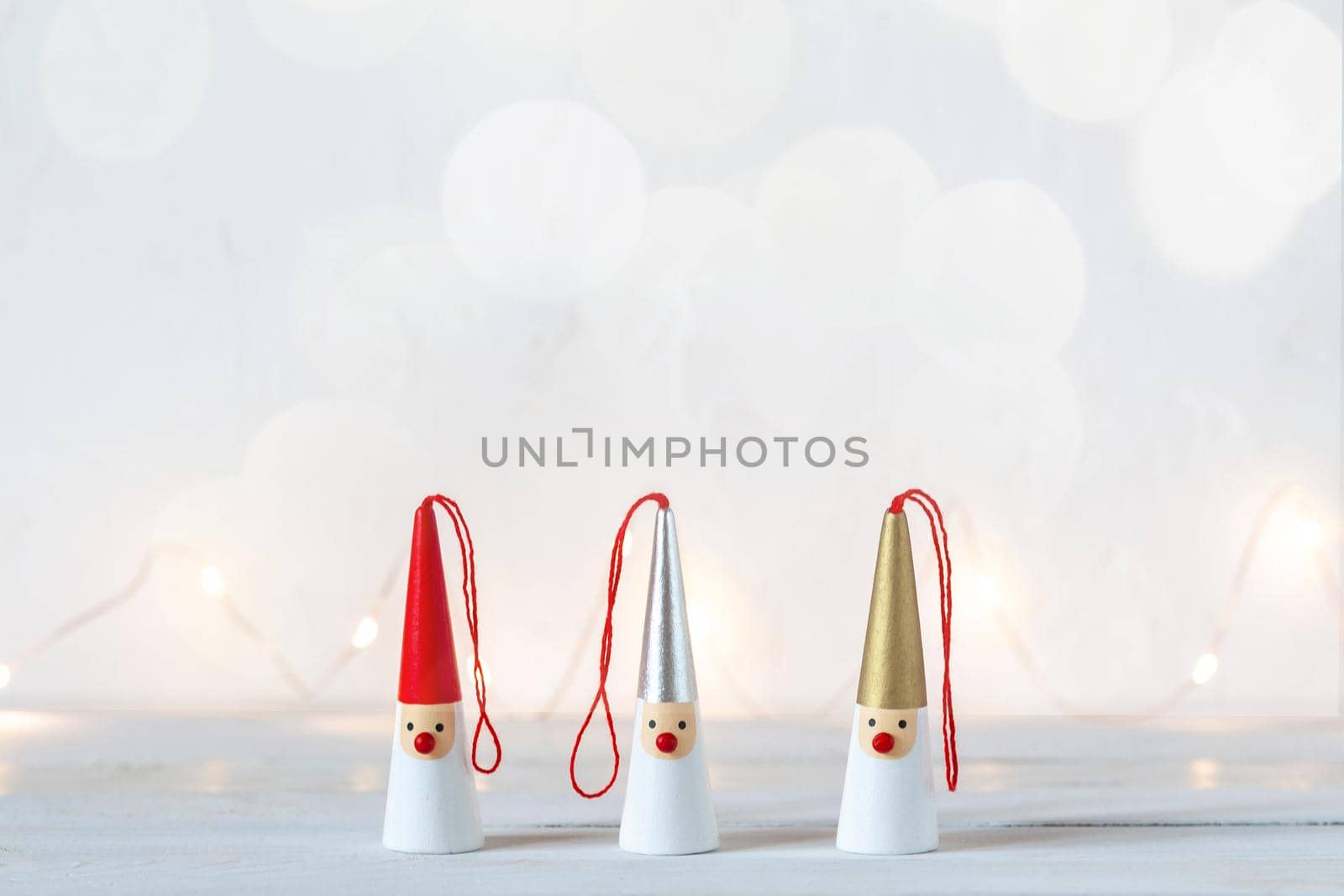 three Santa Clauses figurines on a white background, garland lights, side view, copy space