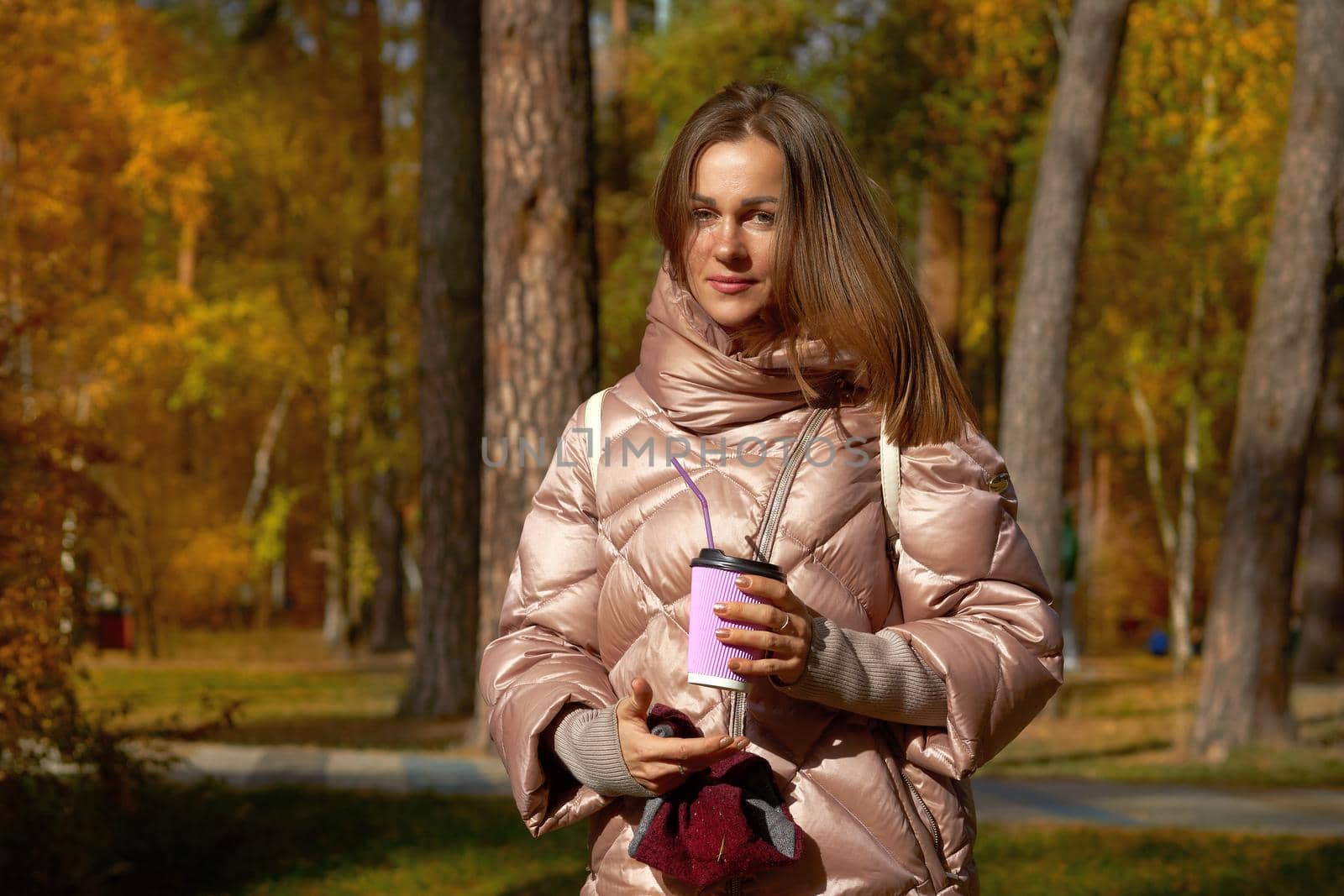 Woman in a pink jacket with a glass of coffee tea in autumn park by jovani68