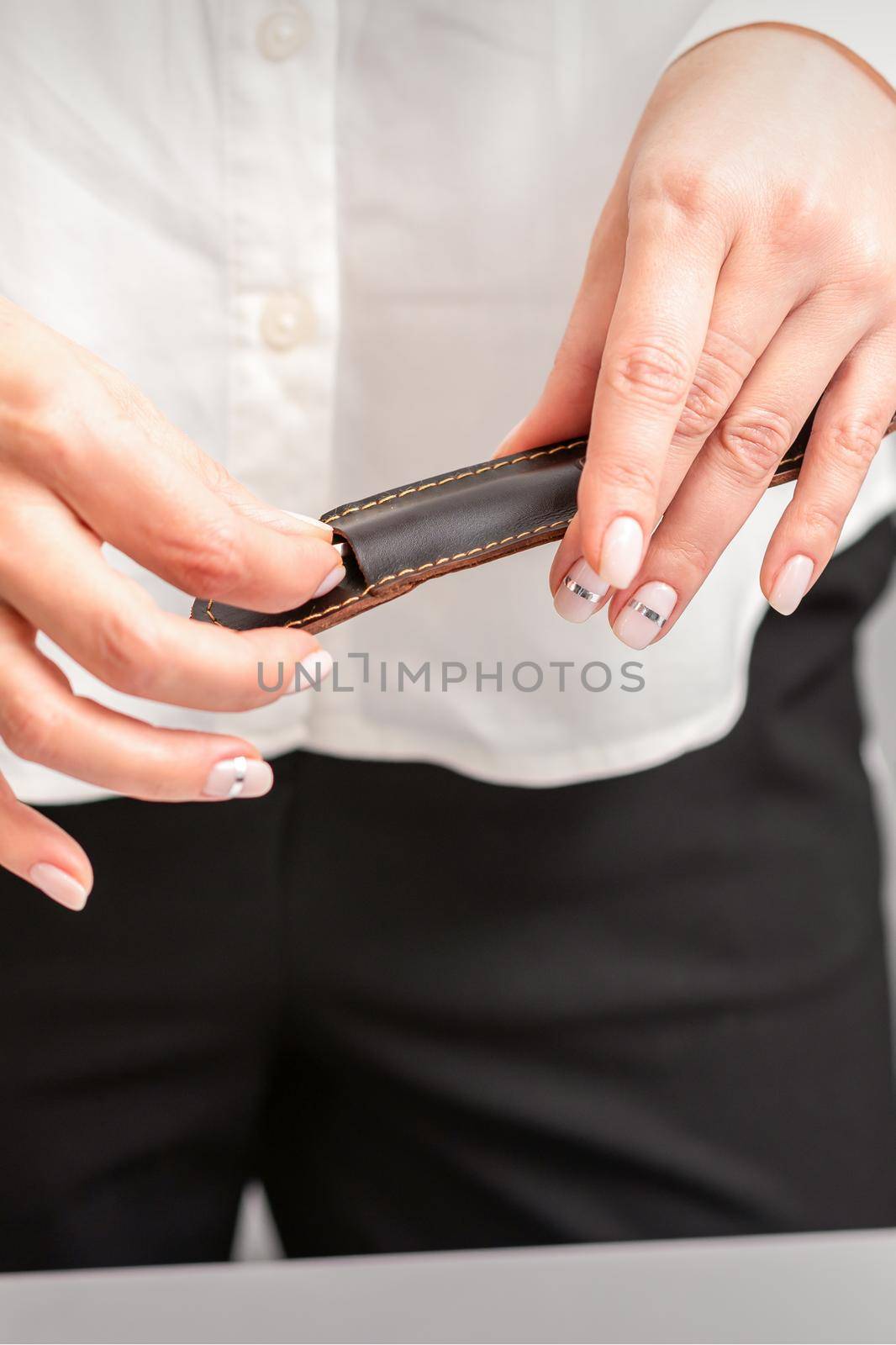 Manicured hands and tools for a manicure. Hands of manicurist take off instrument for a manicure from the leather case in a nail salon