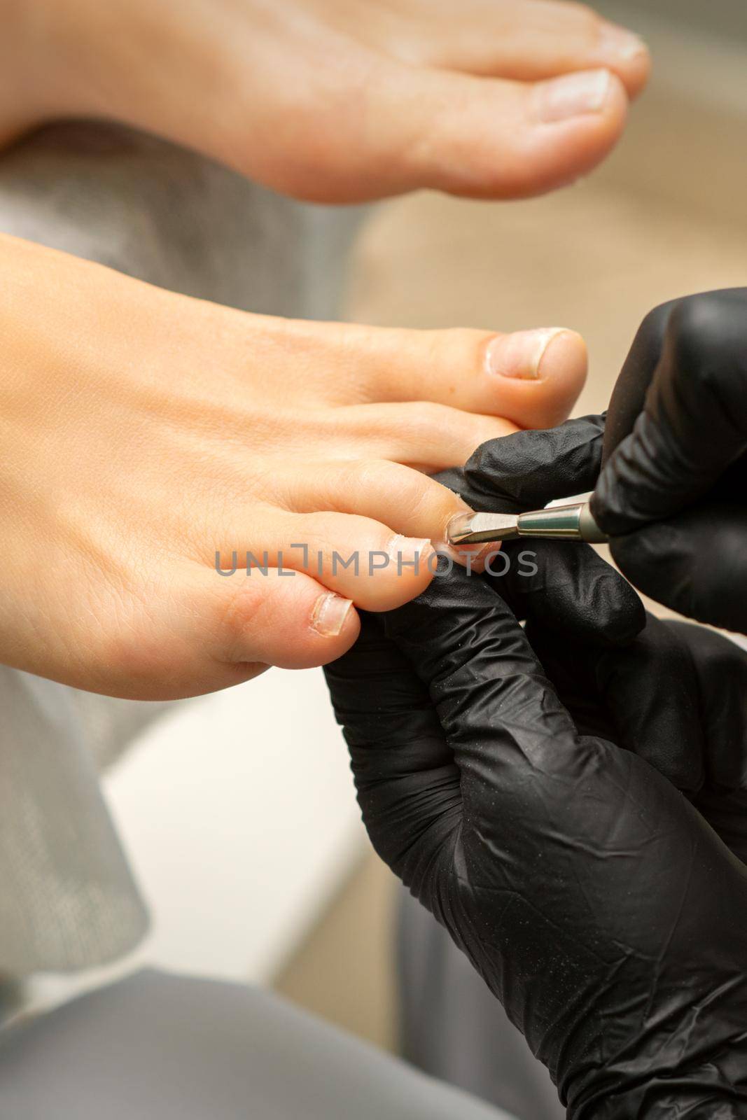 Cuticle Removal on Toes. Hands in black gloves of pedicure master remove cuticle on female toes by pusher. by okskukuruza