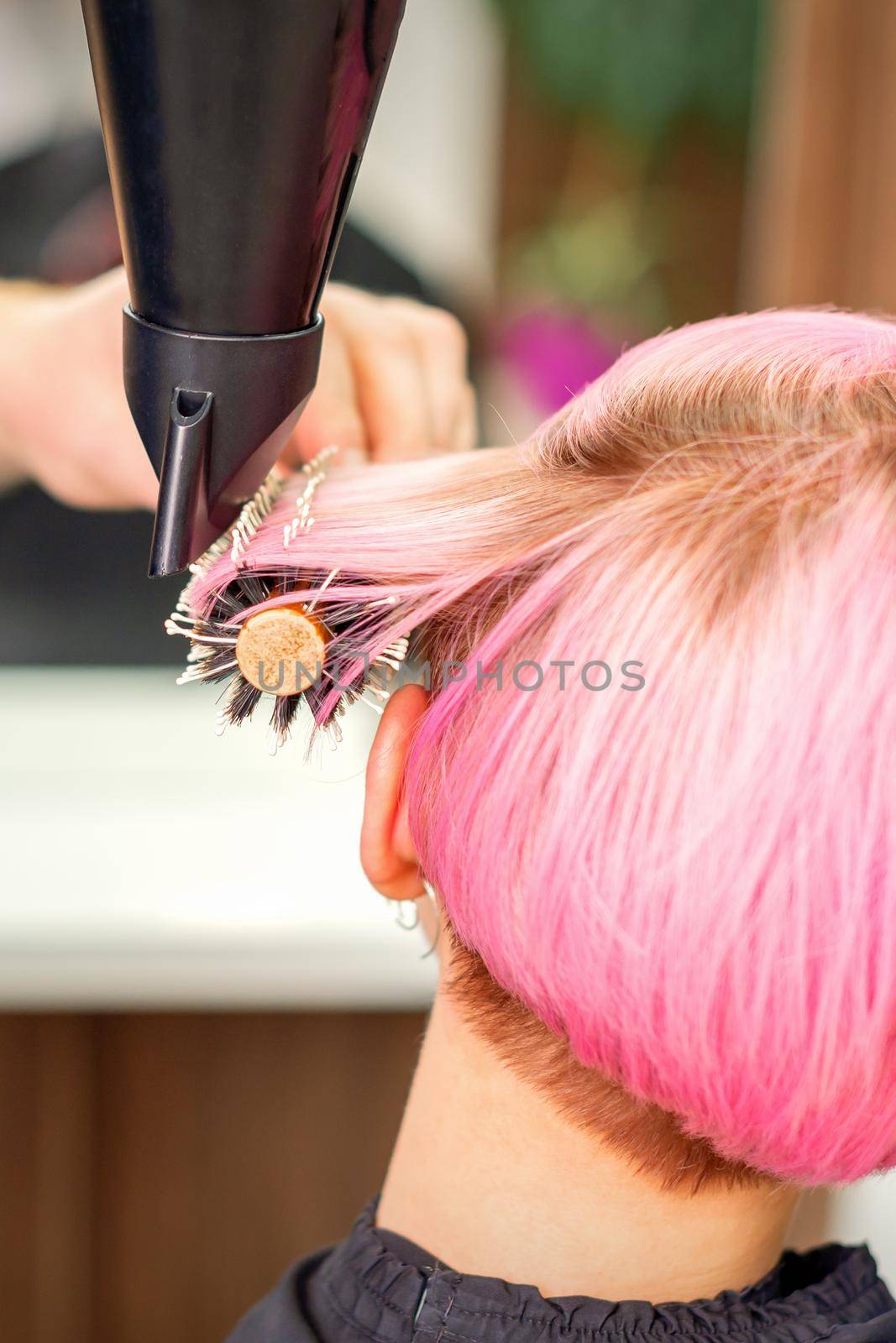 A professional hairdresser is drying long red hair with a hair dryer and round brush, close up. by okskukuruza