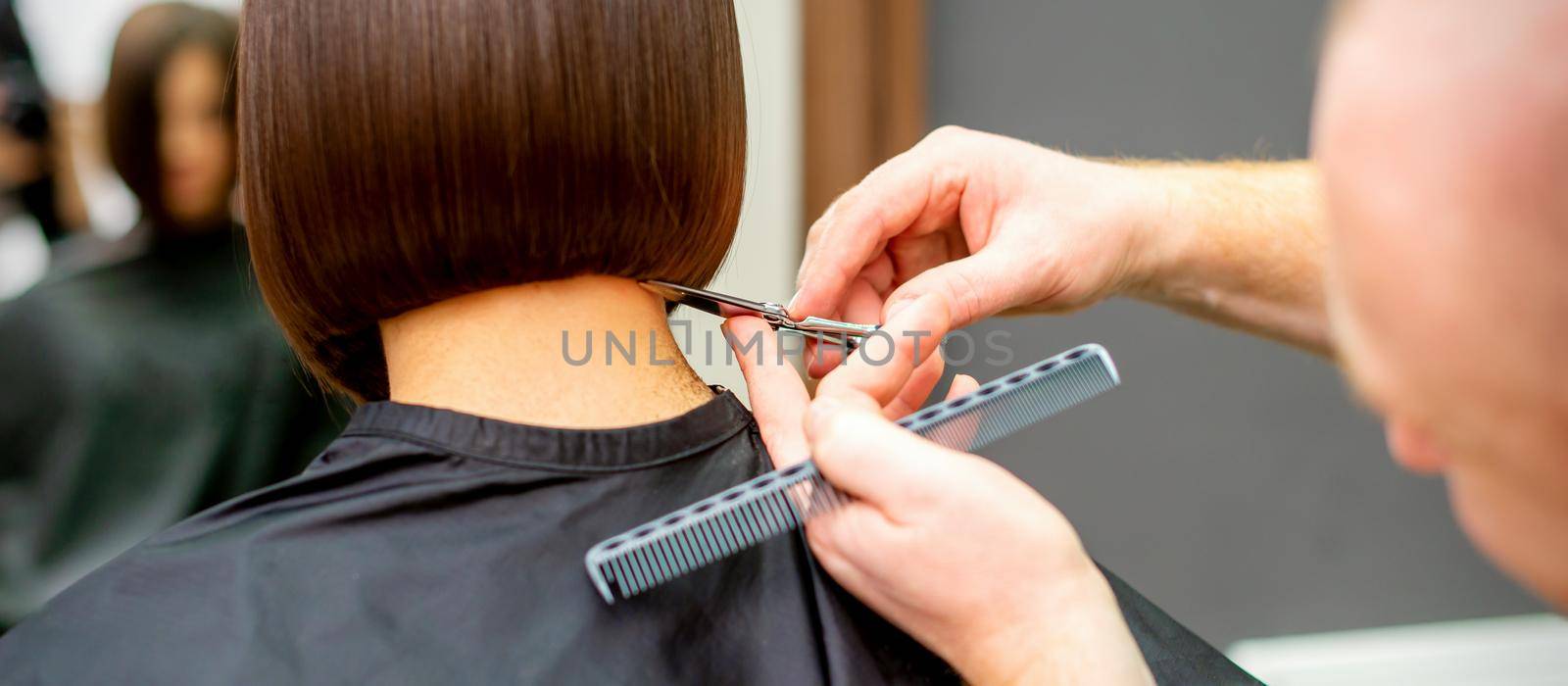 The hairdresser cuts the hair of a brunette woman. Hairstylist is cutting the hair of female client in a professional hair salon, close up