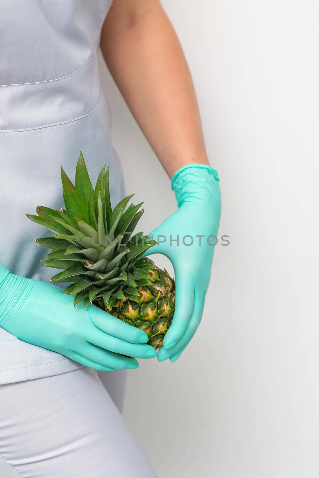 Young beautician wearing blue gloves in uniform with pineapple covers an intimate area on a white background, bikini zone depilation concept