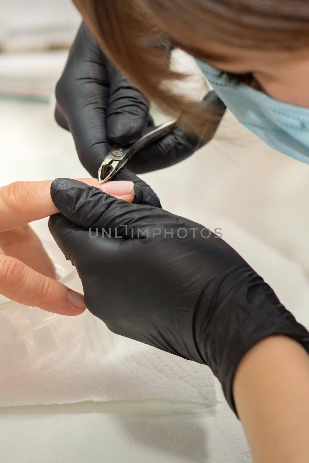 Nail master removing nails cuticle with a nipper, manicure hygiene in a beauty salon