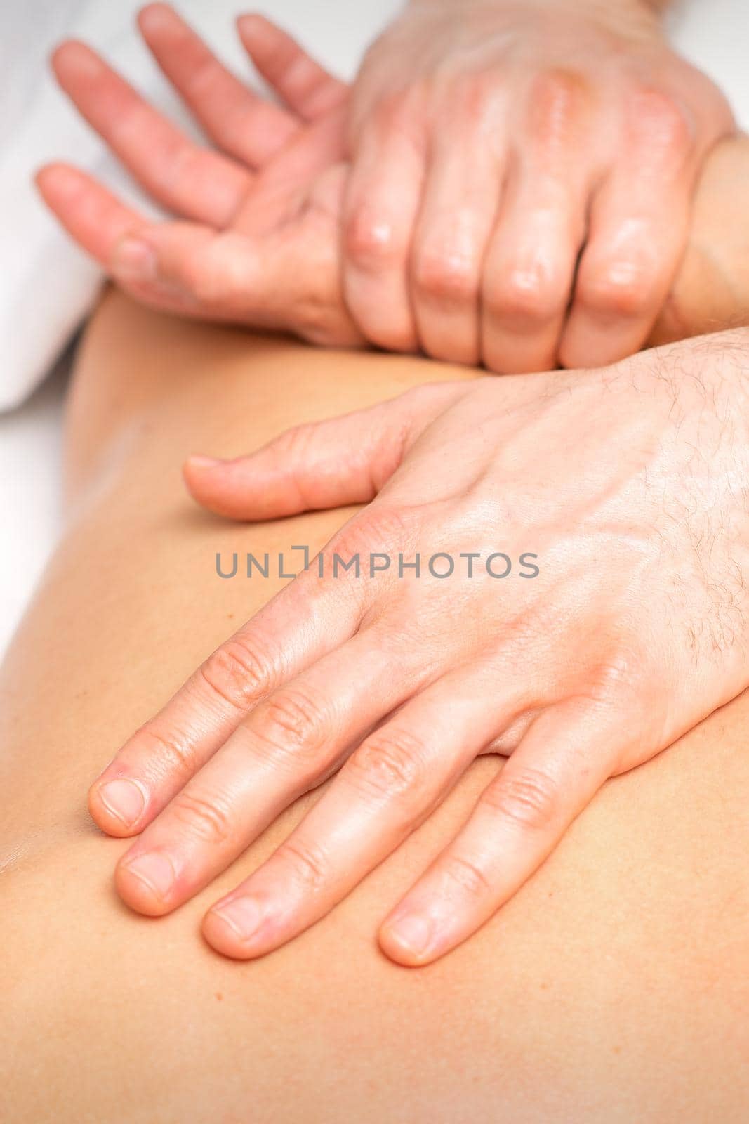 A male physiotherapist stretches the arms on the back of a man lying down, close up