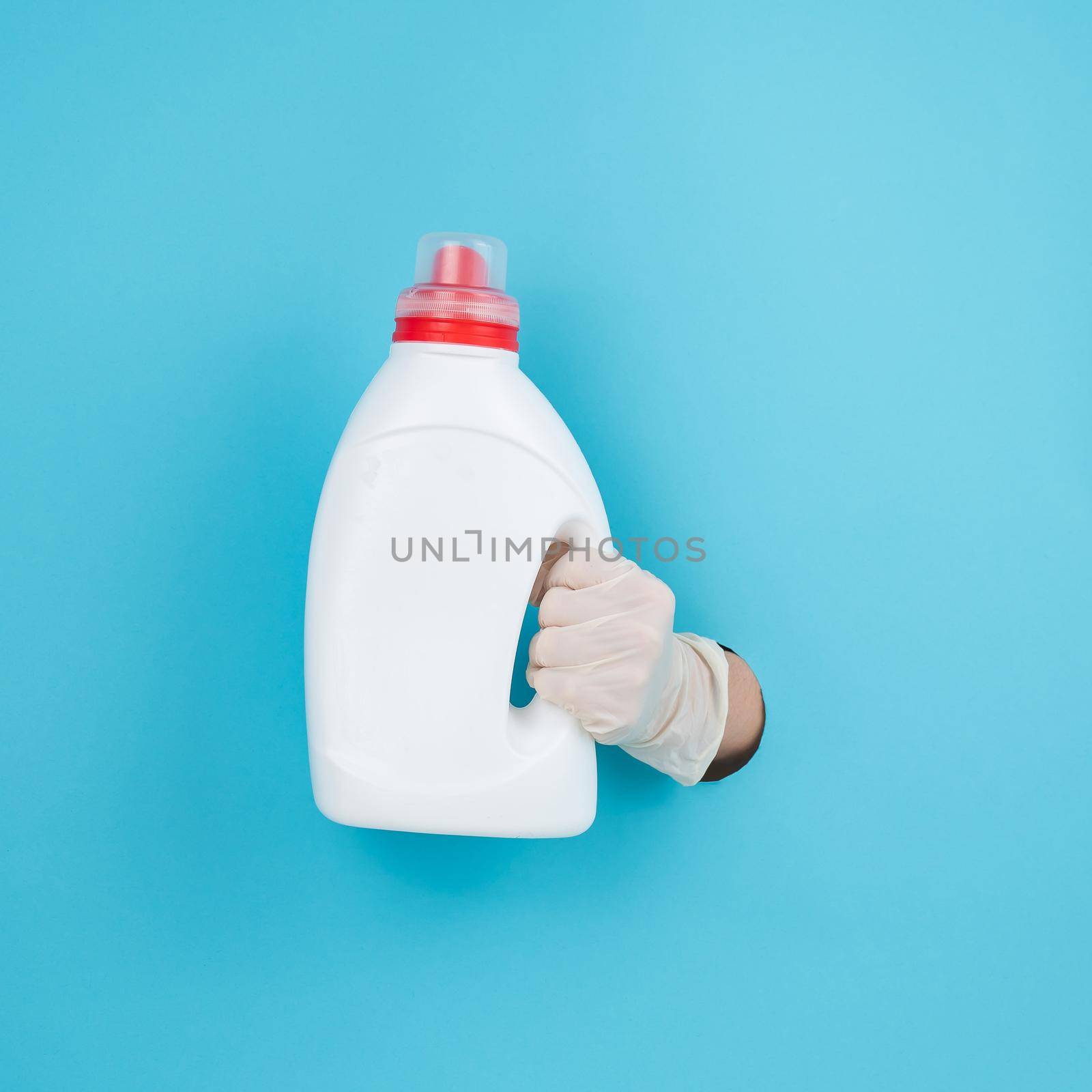 A woman is holding a white bottle of detergent. Woman's hand sticking out of blue paper background. by mrwed54