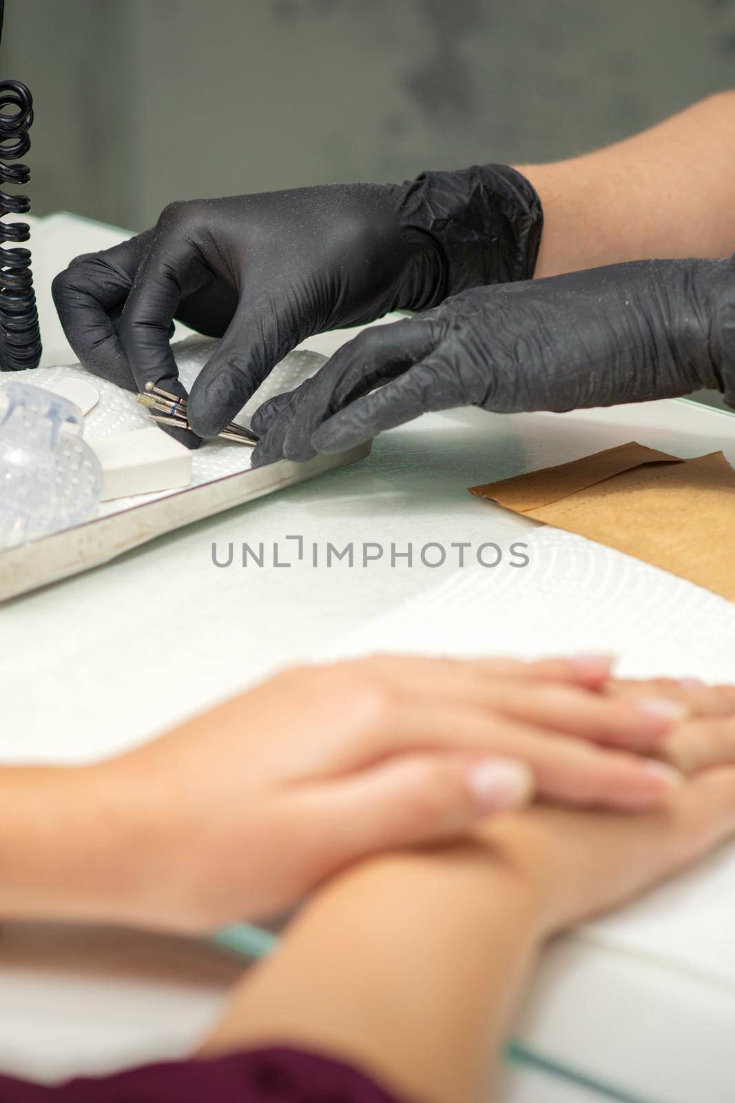 Hands in black gloves of manicurist preparing special nail file equipment for manicure treatment in a beauty salon. by okskukuruza