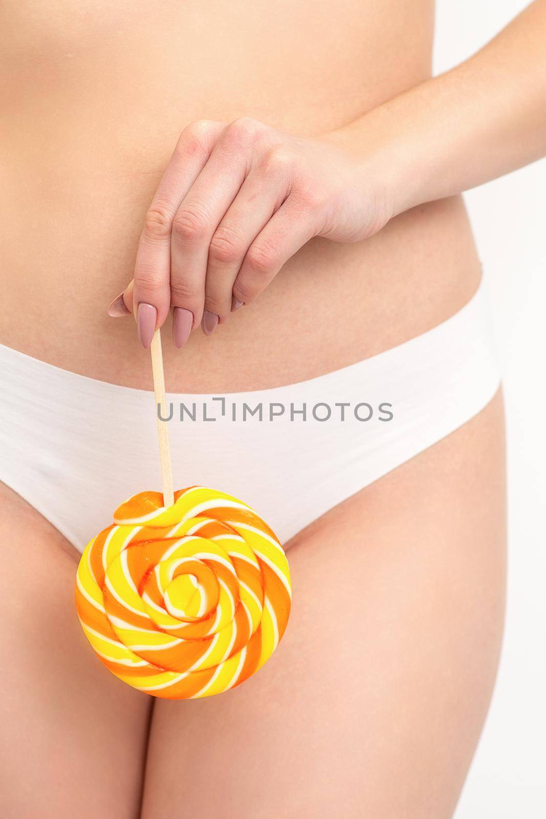 Hand of a woman wearing white panties holding lollipop on a stick covering the intimate area, the concept of intimate depilation, problems of intimate hygiene