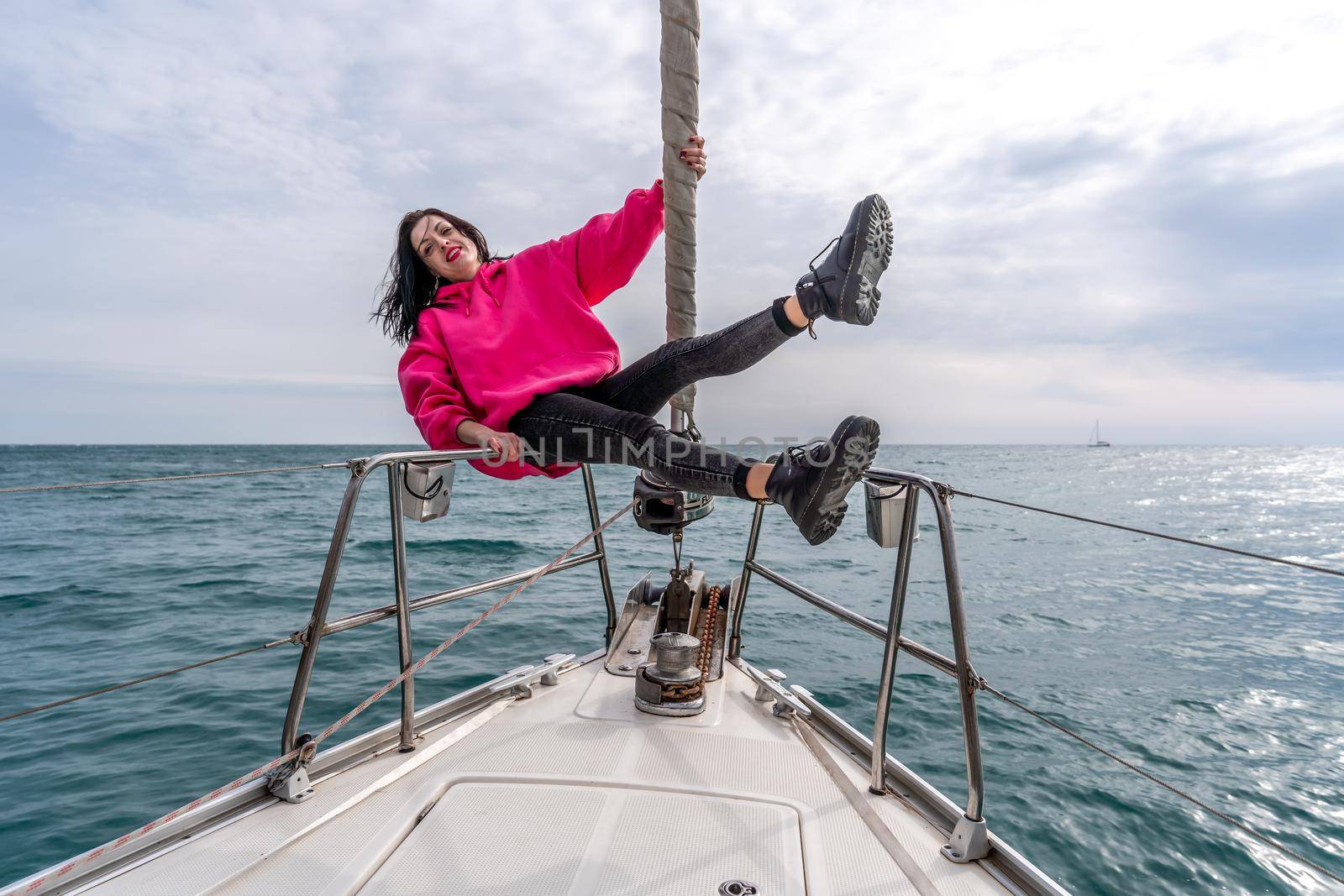 Woman standing on the nose of the yacht at a sunny summer day, breeze developing hair, beautiful sea on background.