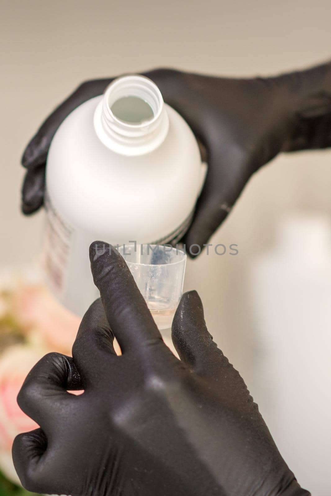 A hairdresser in black gloves is preparing hair dye with a bottle in a hair salon, close up. by okskukuruza
