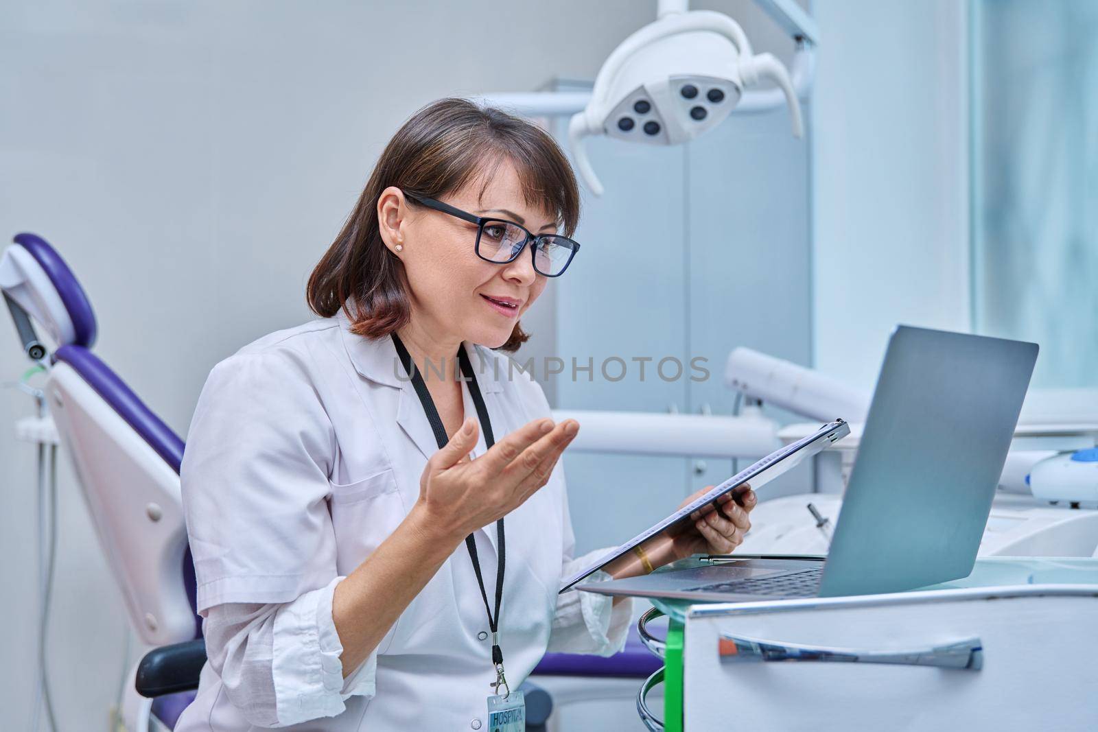 Doctor dentist working in office, using laptop clipboard, making video call conference, talking consulting patients online. Technology, medicine, dentistry, dental health care concept