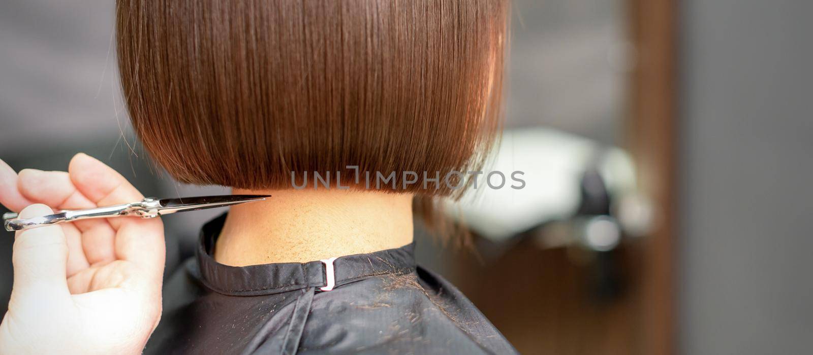 The hairdresser cuts the hair of a brunette woman. Hairstylist is cutting the hair of female client in a professional hair salon, close up