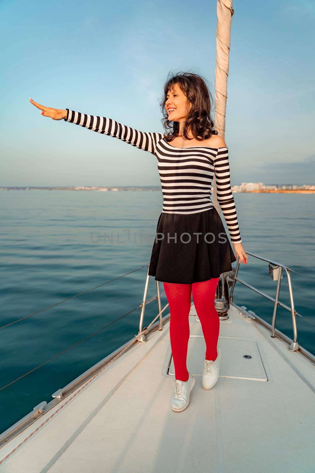 Woman standing on the nose of the yacht at a sunny summer day, breeze developing hair, beautiful sea on background by Matiunina