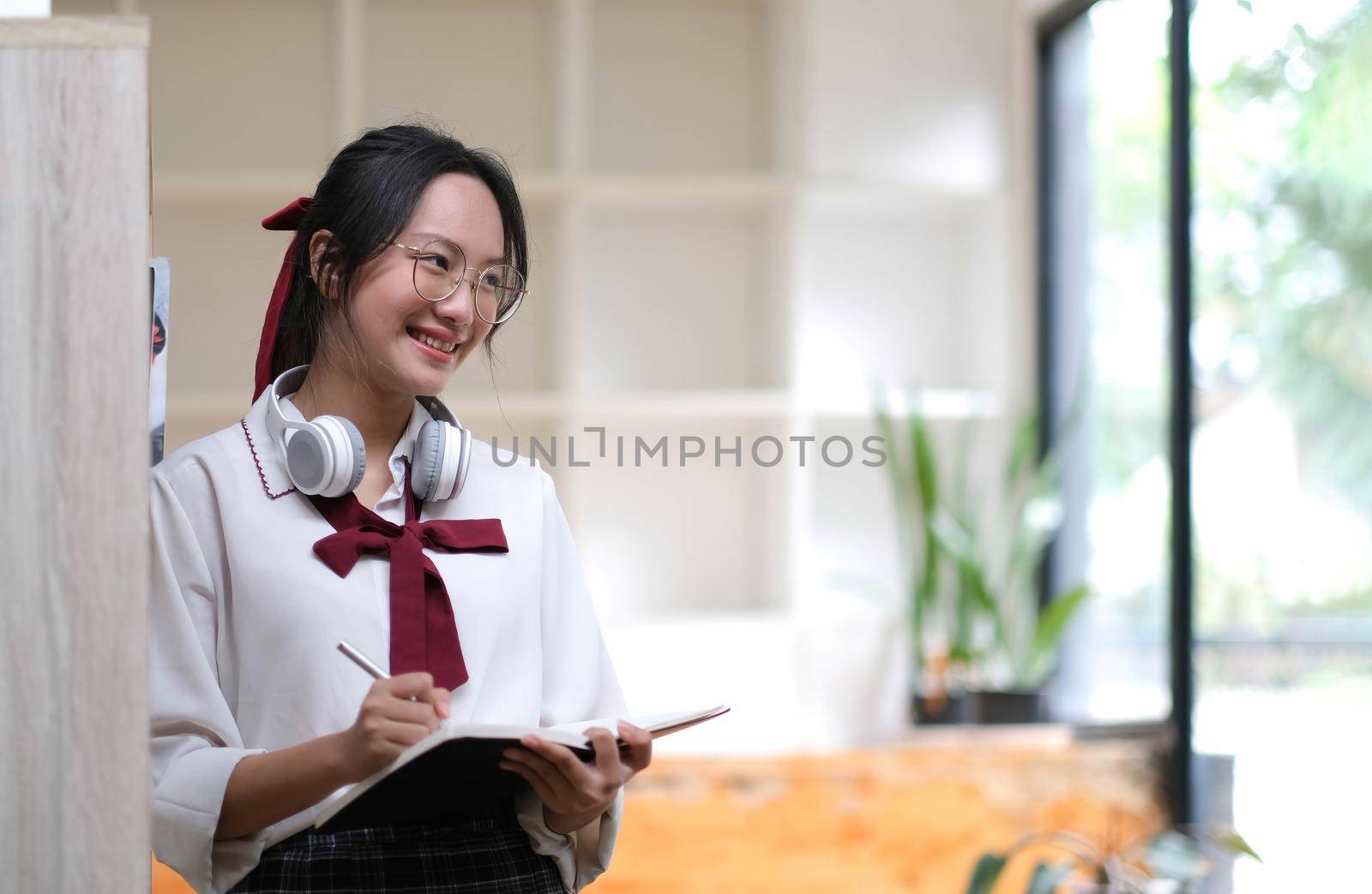 Young asian business woman is standing at a desk and taking notes in a notebook. The concept of education and technology. by wichayada