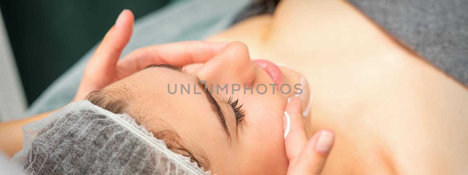 Spa facial skincare. Close-up of a young caucasian woman getting spa moisturizing face massage treatment at beauty spa salon. by okskukuruza