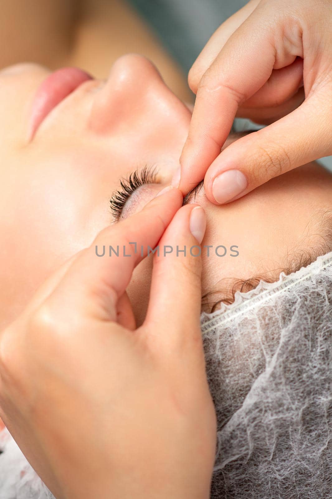 Manual sculpting face massage in the spa. Fingers of beautician make facial massage eyebrow of a young woman in cosmetology clinic, close up. by okskukuruza