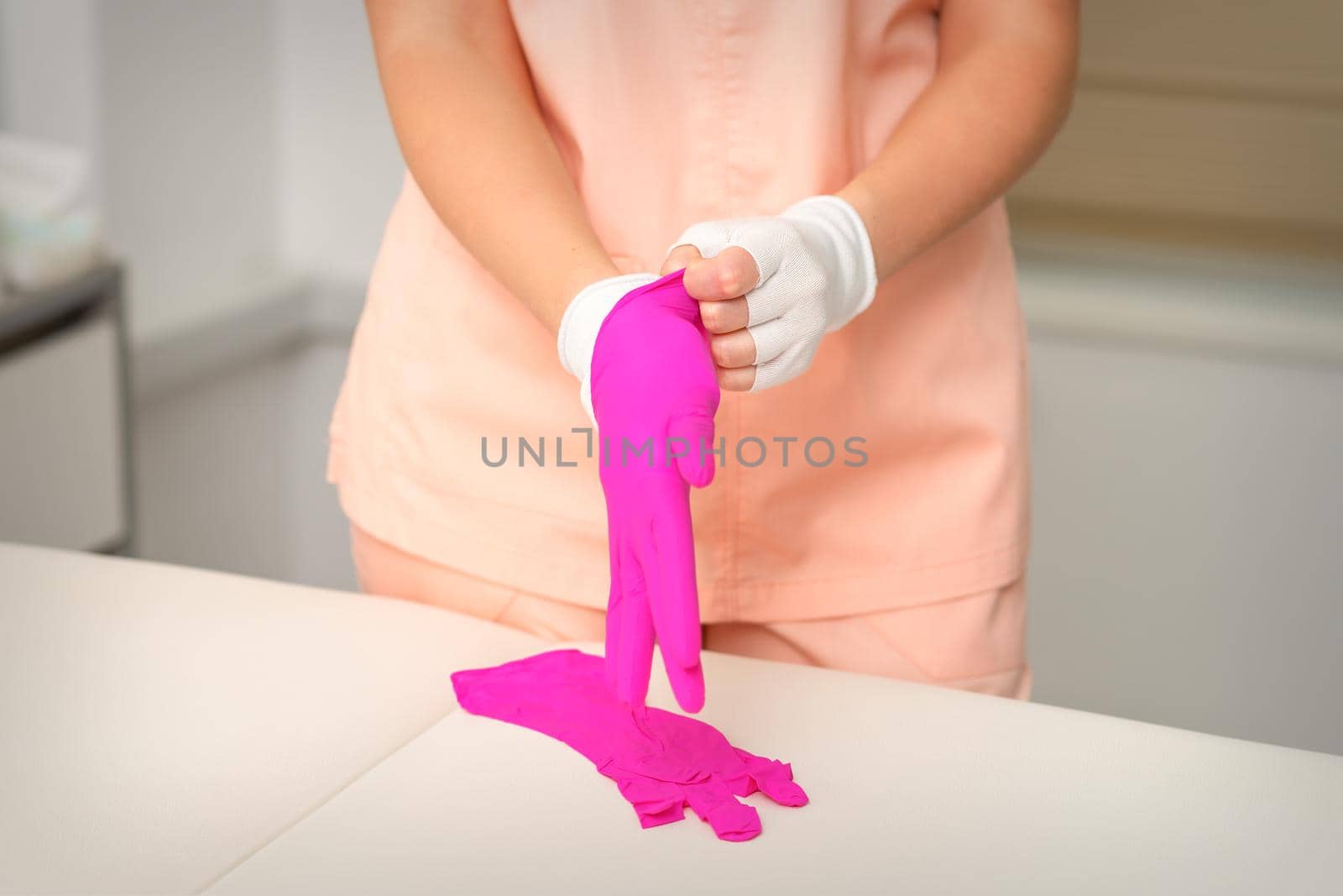 Hands of beautician put on rubber pink gloves prepare to receive clients. by okskukuruza