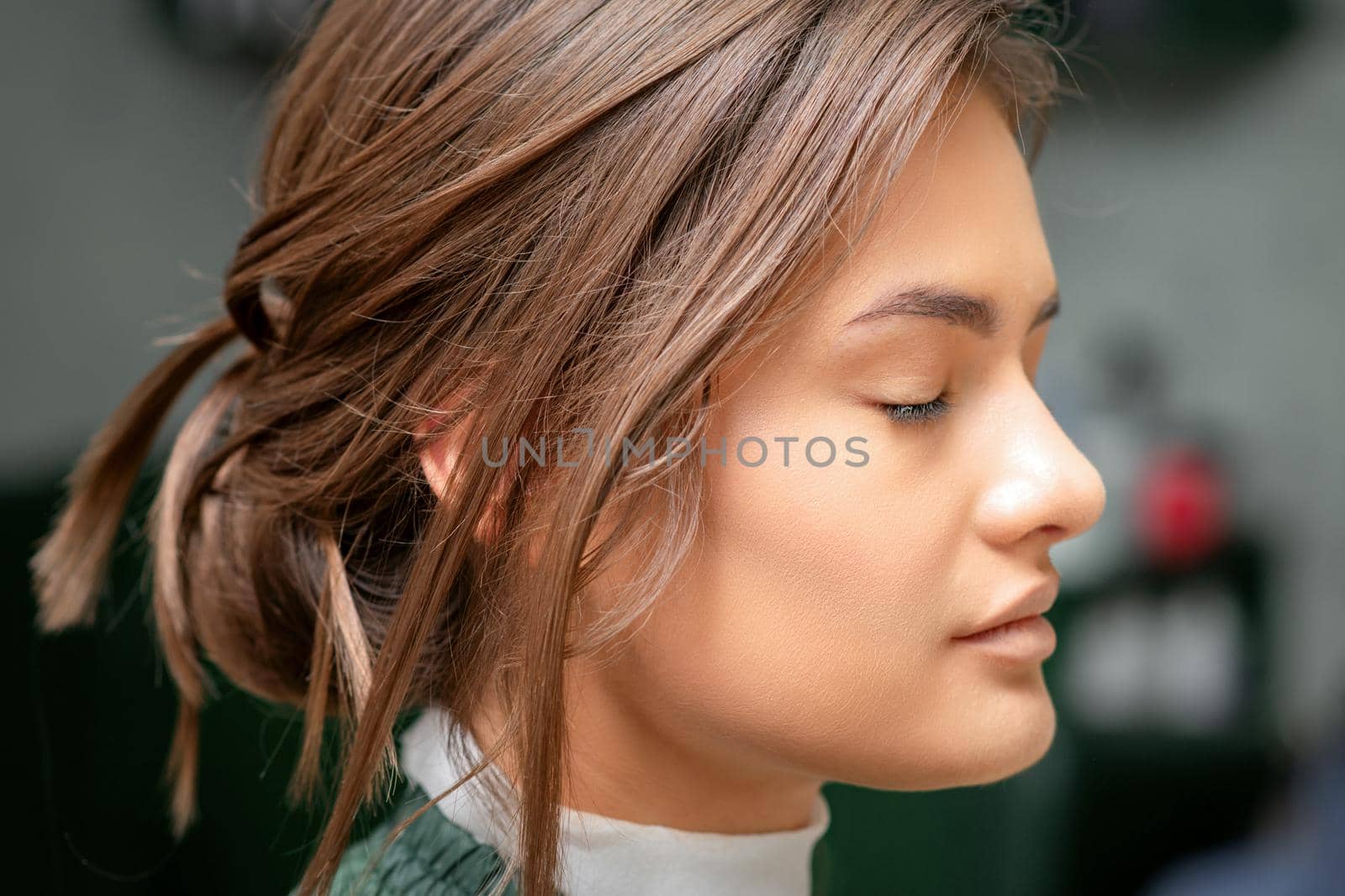Portrait of a sensual young caucasian woman with closed eyes showing makeup tan on her face and hairstyle in a beauty salon