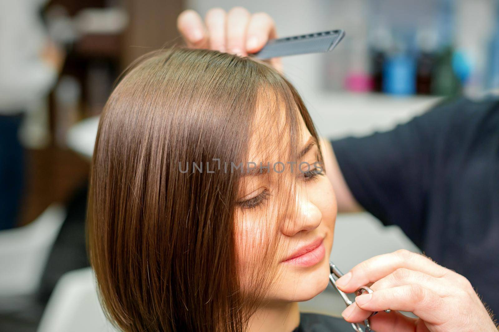 The hairdresser cuts the hair of a brunette woman. Hairstylist is cutting the hair of female client in a professional hair salon, close up