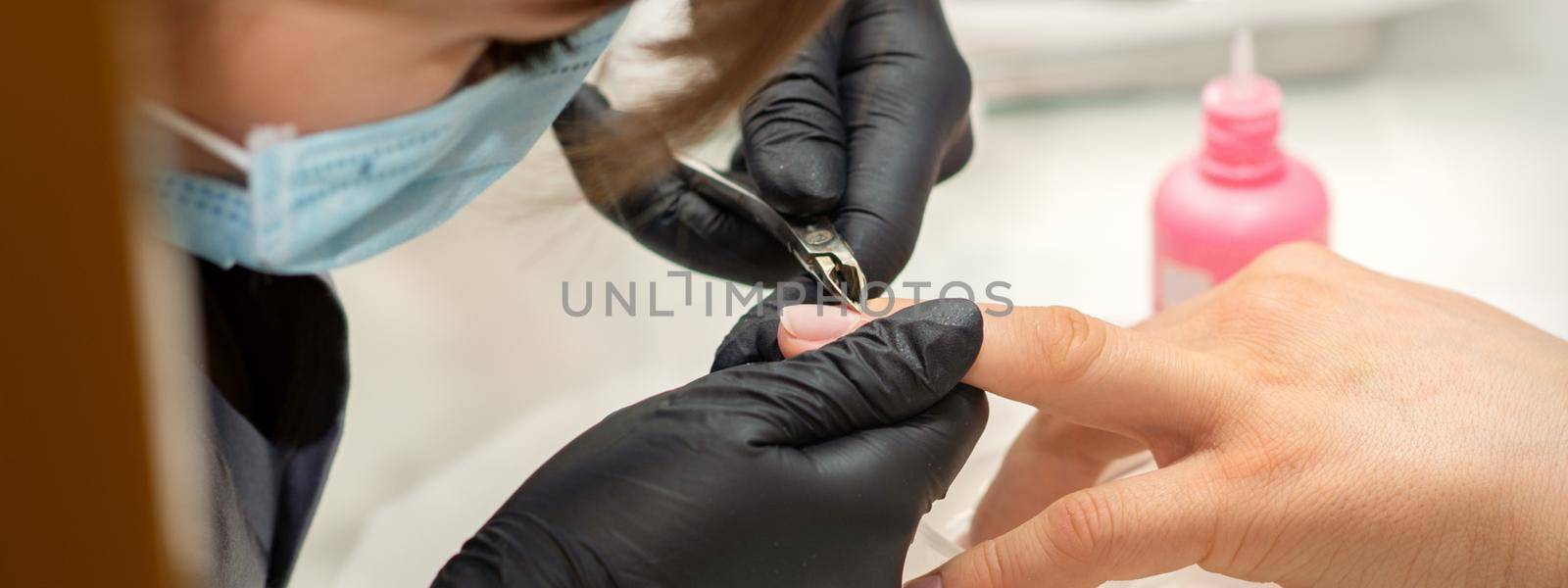 Nail master removing nails cuticle with a nipper, manicure hygiene in a beauty salon