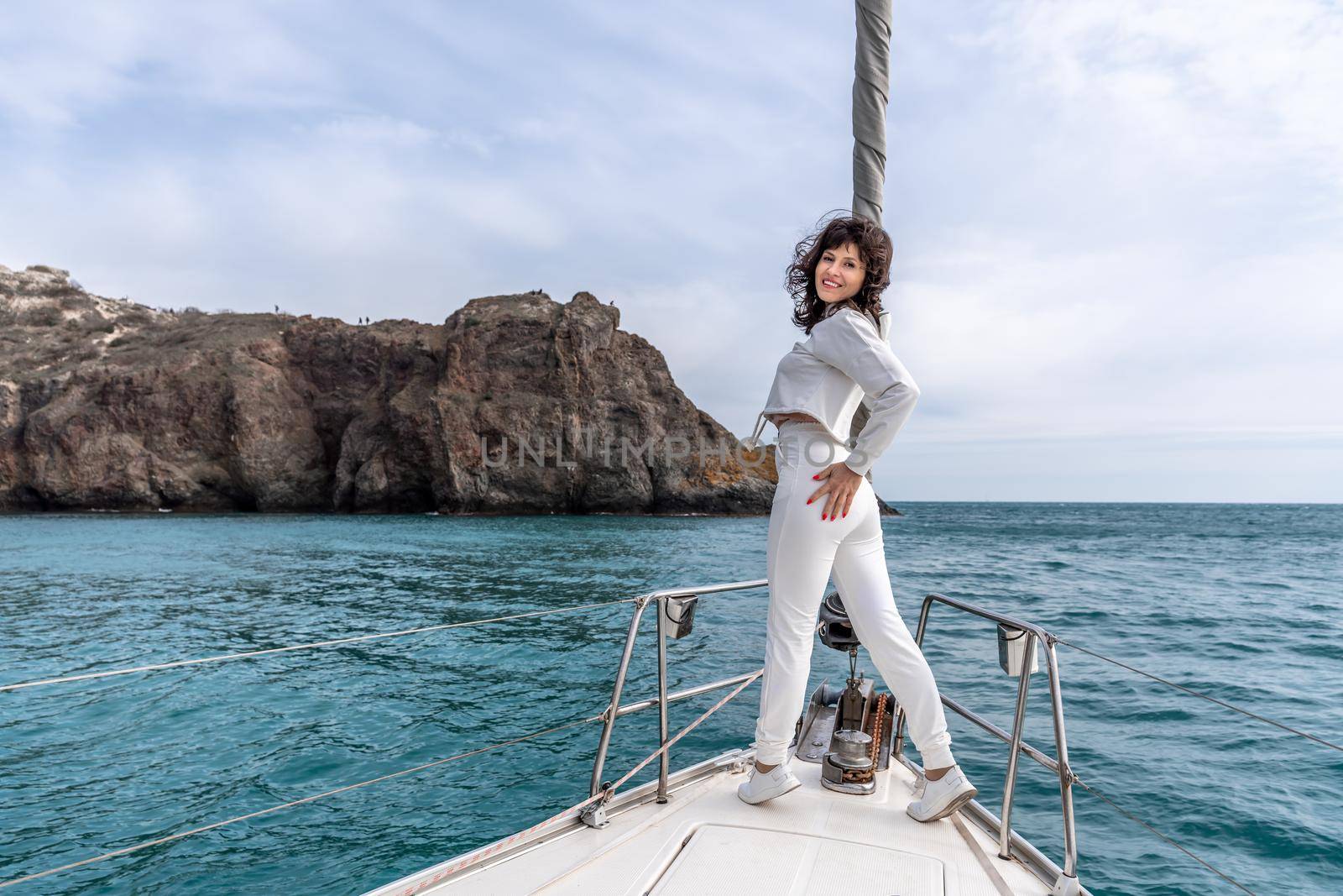 Woman standing on the nose of the yacht at a sunny summer day, breeze developing hair, beautiful sea on background.