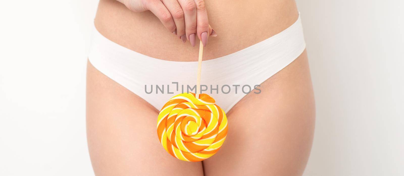 Hand of a woman wearing white panties holding lollipop on a stick covering the intimate area, the concept of intimate depilation, problems of intimate hygiene