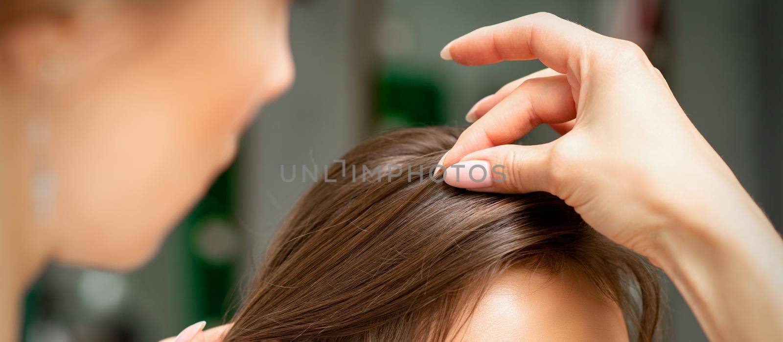 A hairdresser is making the hairstyle of a young brunette woman in a hair salon, close up. by okskukuruza