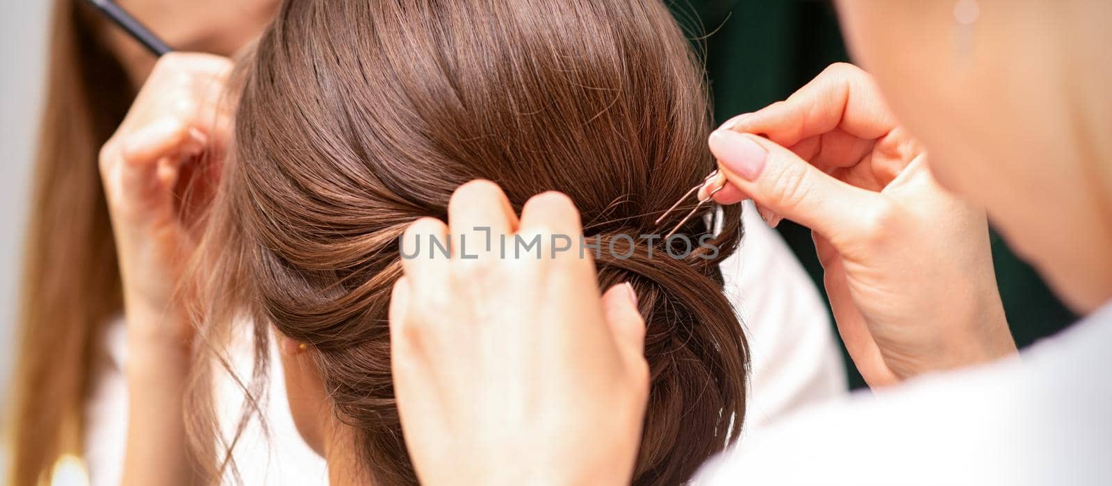 A hairdresser is making the hairstyle of a young brunette woman in a hair salon, close up. by okskukuruza