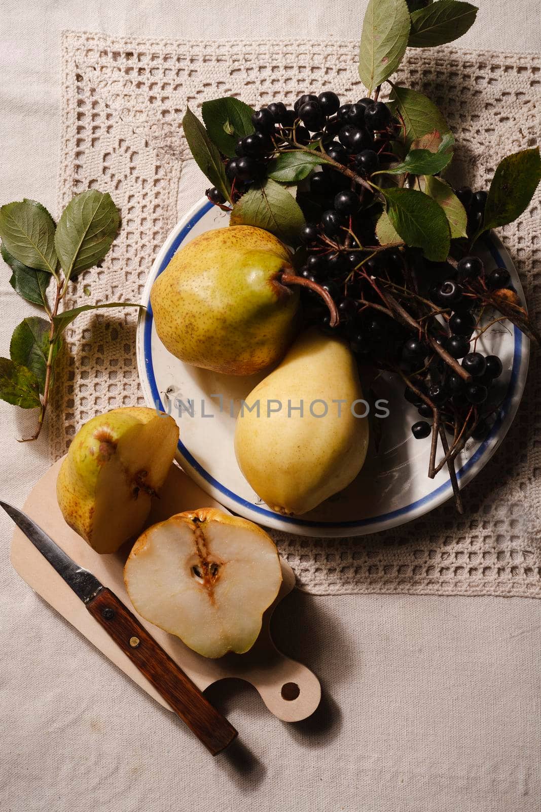 Ripe yellow pears and chokeberry on white plate prepared for jam cooking on rustical tablecloth, top view, flat lay.