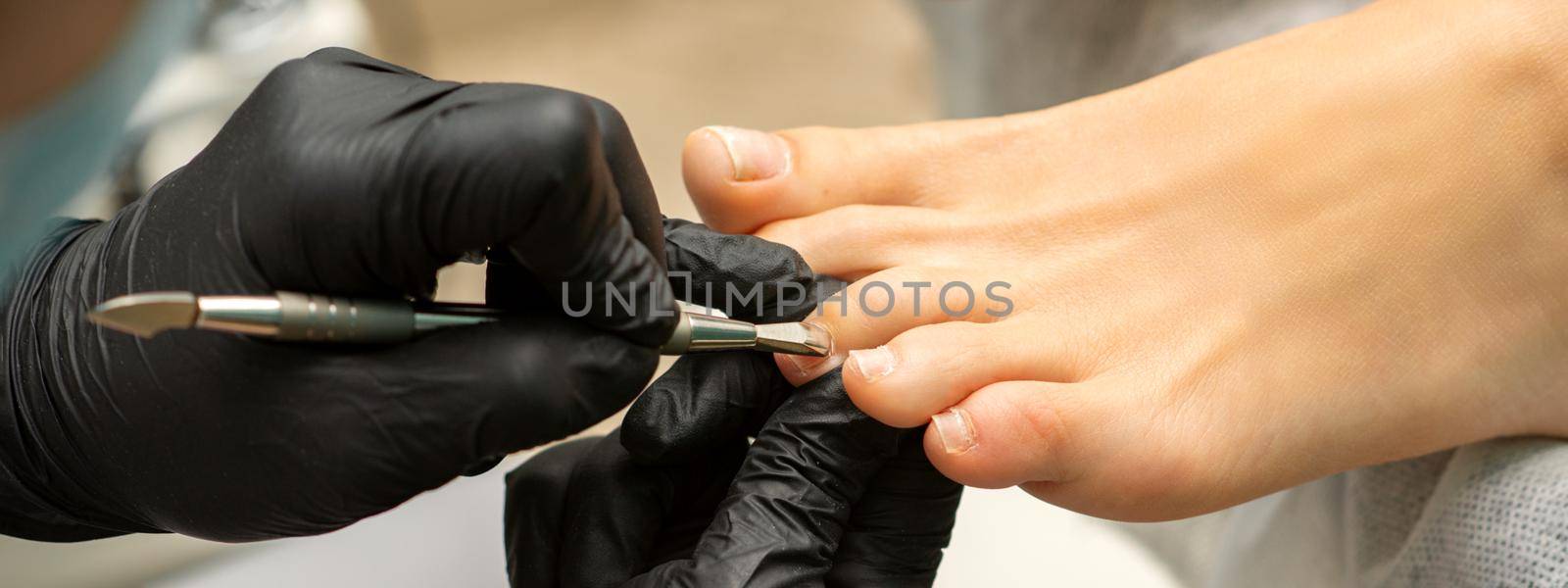 Cuticle Removal on Toes. Hands in black gloves of pedicure master remove cuticle on female toes by pusher. by okskukuruza