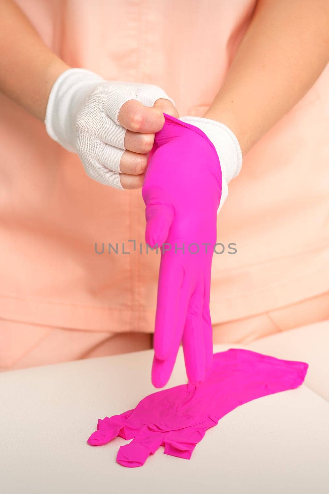 Hands of beautician put on rubber pink gloves prepare to receive clients