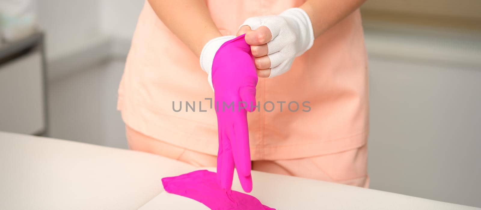 Hands of beautician put on rubber pink gloves prepare to receive clients