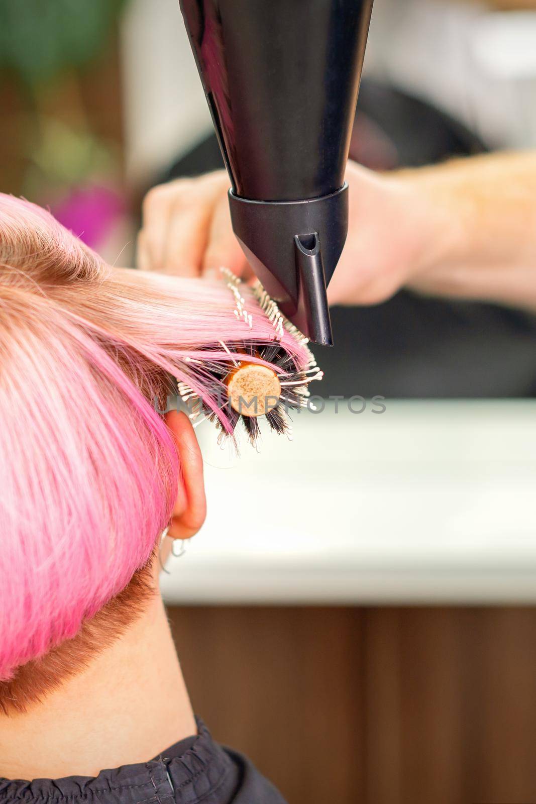 A professional hairdresser is drying long red hair with a hair dryer and round brush, close up