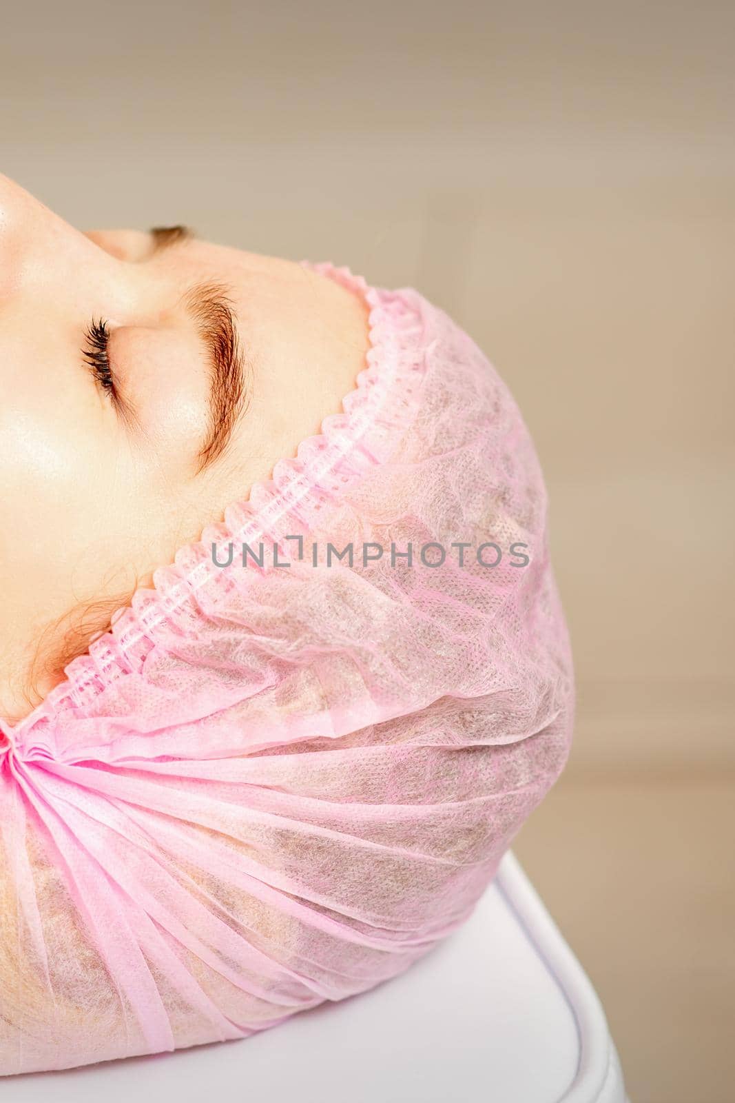 Side view of a young caucasian woman in a medical cap lying with closed eyes waiting for the cosmetic procedure in a beauty salon. by okskukuruza